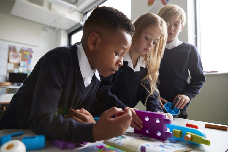 Close up of three primary school children working together with toy construction blocks in a classroom,